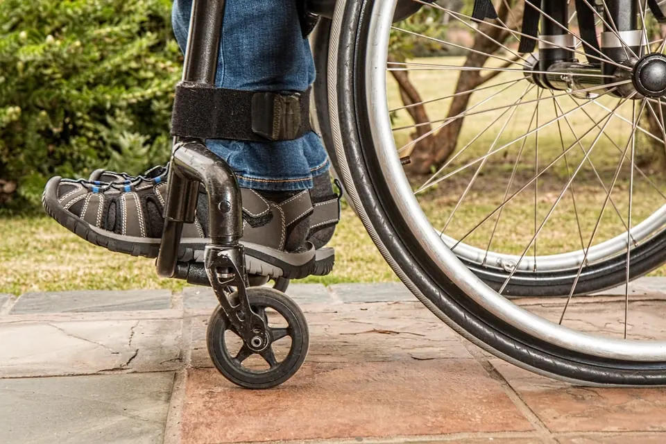 Close-up of a wheelchair wheel and footrest on a stone path